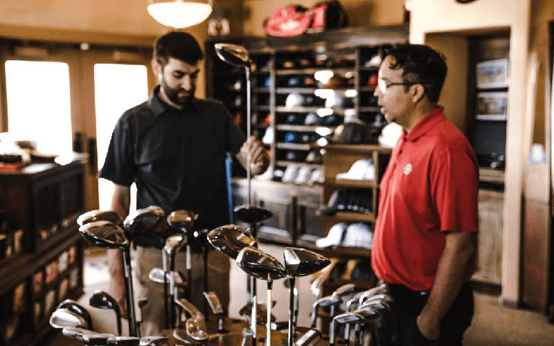 Two men in a golf pro shop discussing club options, representing golf course management and multi-course operations.